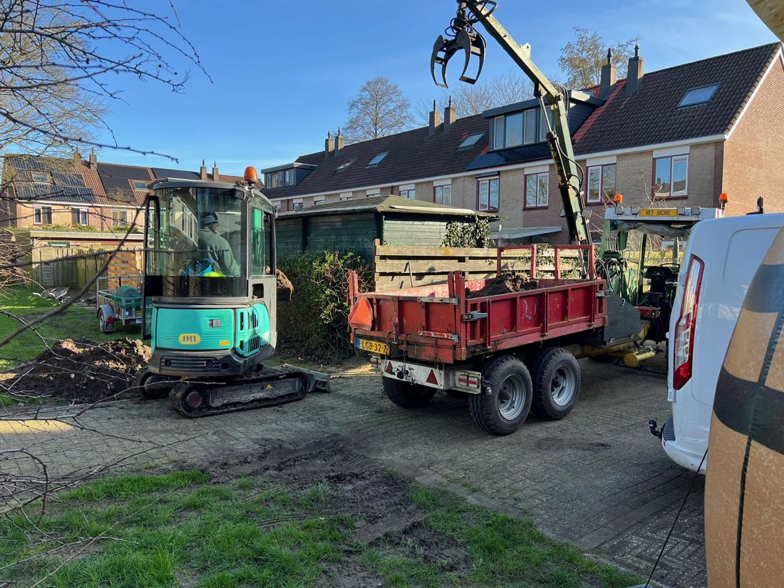 Minigraver met machinist en tractor met kipper en kraan bij een tuinaanleg